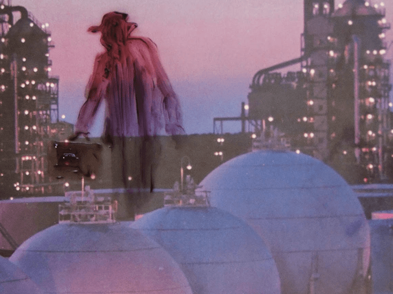Still of a figure with pink hair standing on a rooftop at dusk above a lit city.